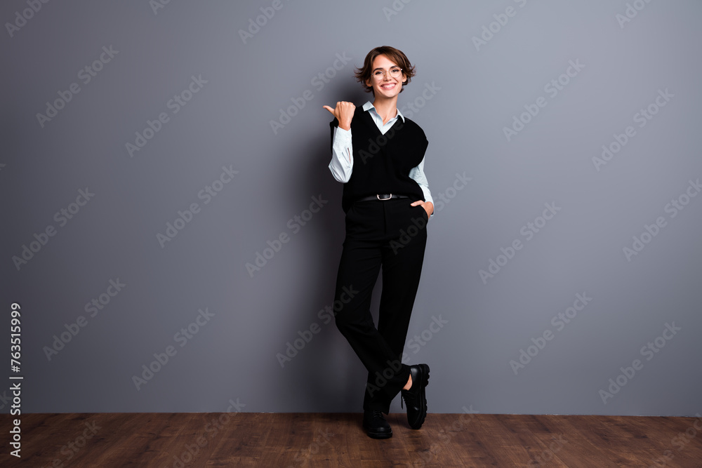 Full length photo of confident cute lady agent dressed black vest eyewear showing thumb empty space isolated grey color background