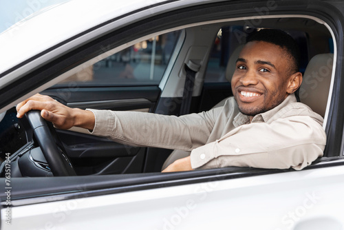A cheerful young man driving a new car after purchasing it, sits in the driver's seat of the car. © Home-stock