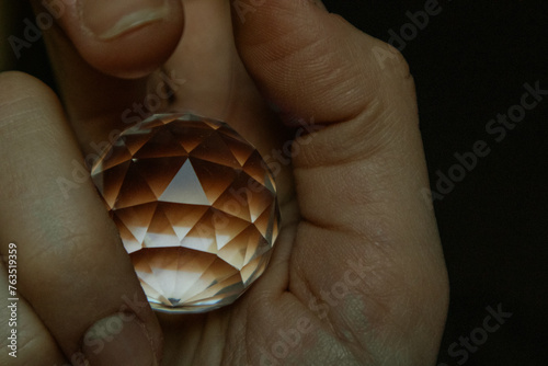 A round brown crystal ball, sphere in human hand close up. A transparent glass globe for spiritual rituals in female hand. A prism to refract light.