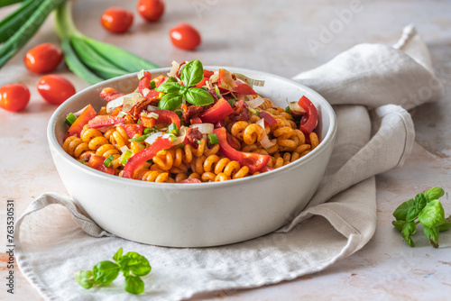 Pasta salad with red pepper, tomatoes, spring onions and basil in a white bowl photo