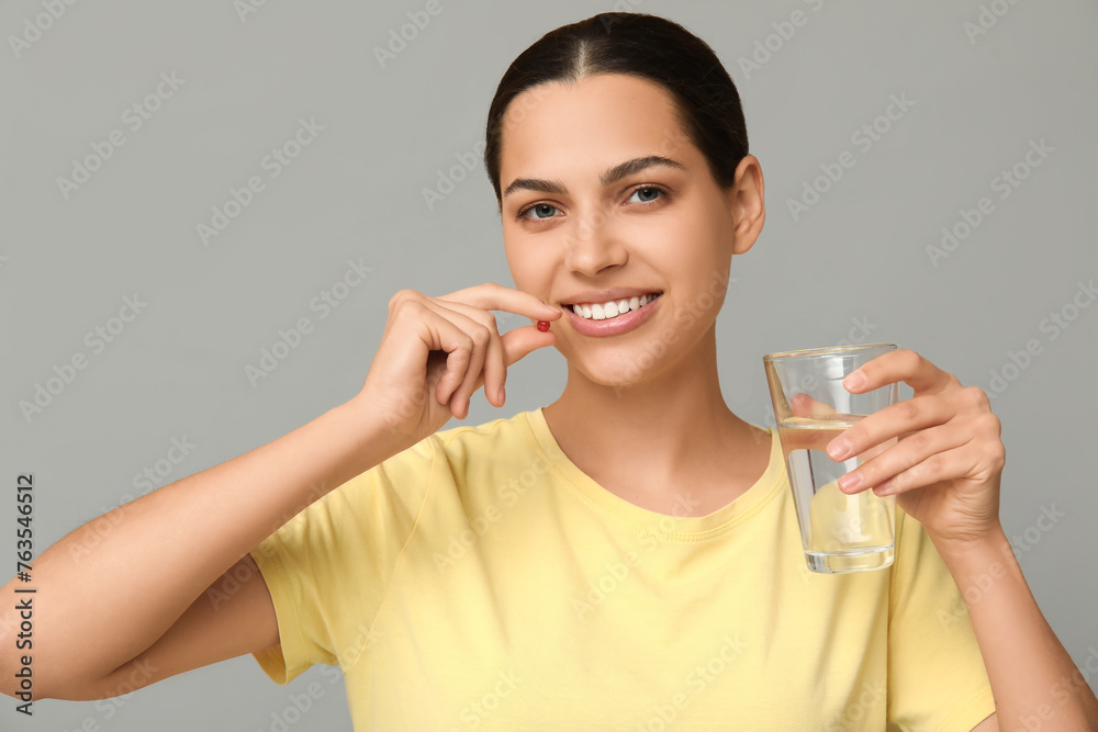 Pretty young woman taking vitamin A capsule on grey background Pretty young woman taking vitamin A capsule on grey background