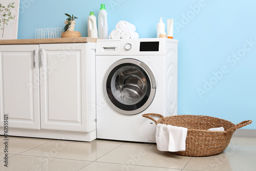 Modern washing machine with basket and cabinet near blue wall. Interior of home laundry room