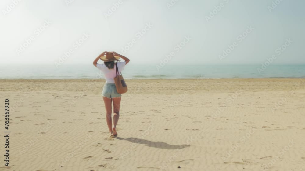 Woman walking sand beach slow motion, ocean waves splashing seashore coastline. Female slim barefoot legs in shorts leave footprints, back view. Outdoor lifestyle travel on summer holiday Woman walking sand beach slow motion, ocean waves splashing seashore coastline. Female slim barefoot legs in shorts leave footprints, back view. Outdoor lifestyle travel on summer holiday