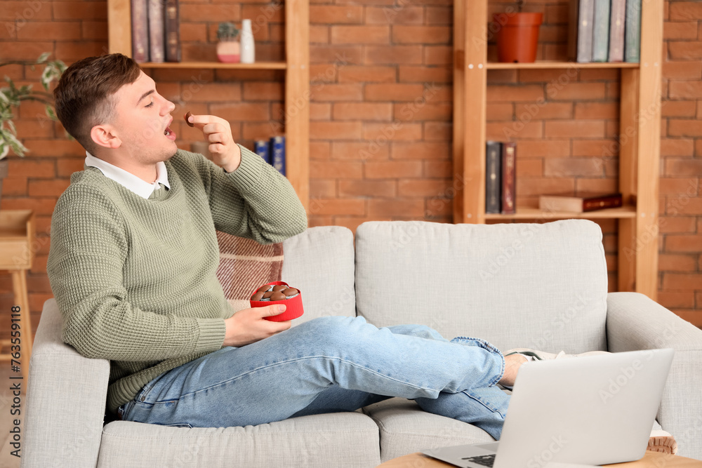 Young man eating heart-shaped chocolate candies at home