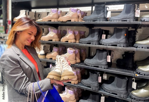 Portrait of smiling beautiful Caucasian woman looking and holding in hands autumn shoes. Positive pretty female buying boots in city mall. Fashion concept. New collection. Season sales