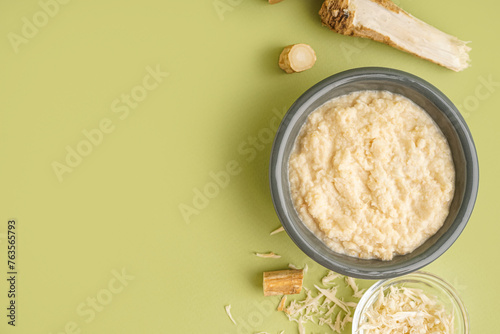 Horseradish sauce in bowls with ground horseradish root on green background. Top view photo