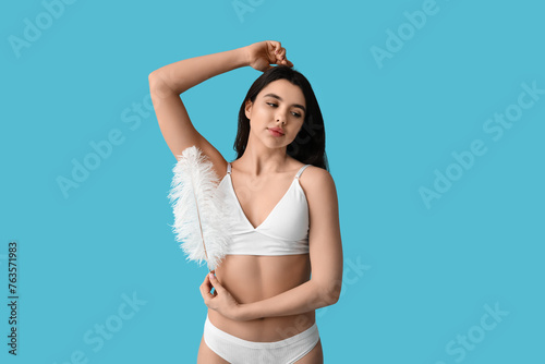 Beautiful young woman with soft feather on blue background. Epilation concept