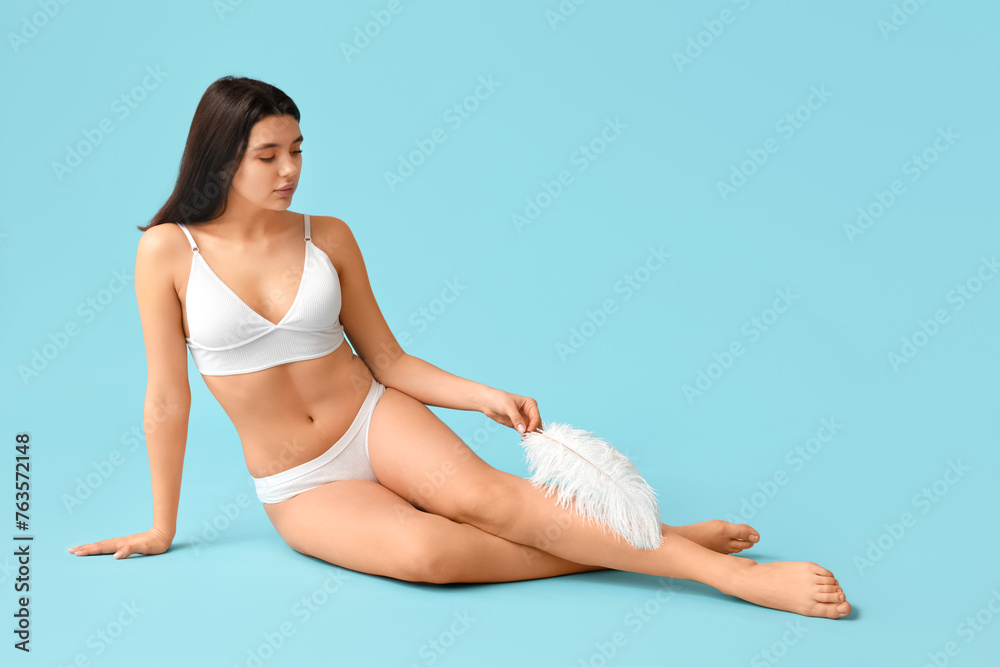 Beautiful young woman with soft feather sitting against blue background. Epilation concept Beautiful young woman with soft feather sitting against blue background. Epilation concept