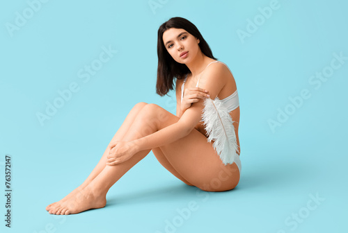 Beautiful young woman with soft feather sitting against blue background. Epilation concept