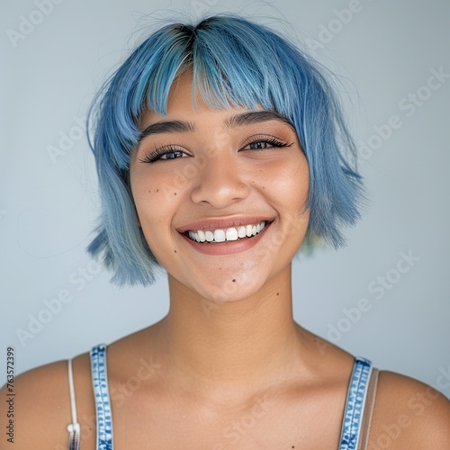 Embrace the cerulean beauty in this skincare portrait of a joyful 20-year-old Latina model showcasing blue hair. Against a soft backdrop, with a luminous filter effect and ambient studio lighting