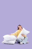 Young woman with soft pillows sitting on lilac background