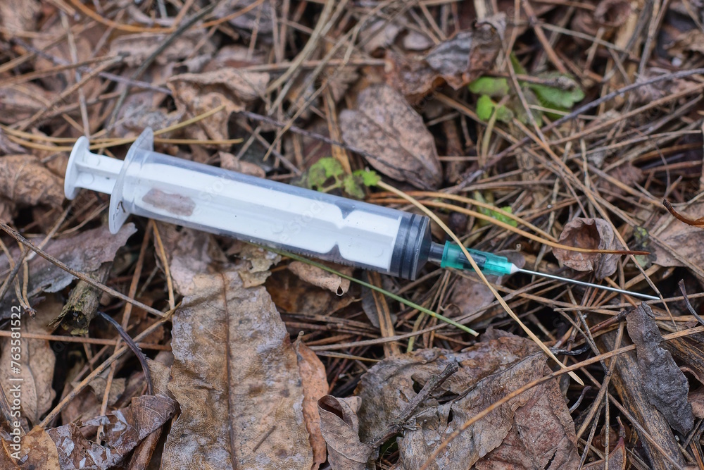 one white syringe with a needle lying on the ground and brown dry leaves in the street