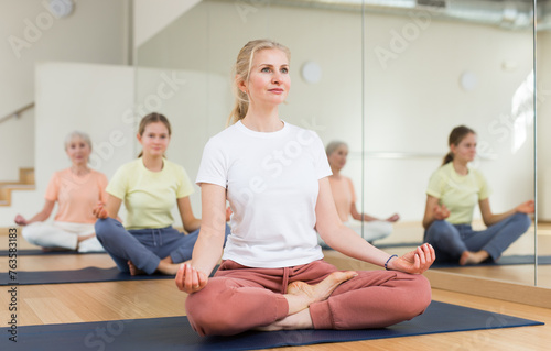 Woman sitting in lotus pose while training yoga in studio.
