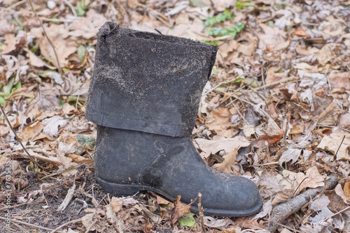 one old torn dirty rubber black boot stands on the ground in the street