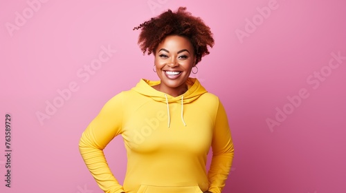 Junge farbige Frau in gelbem Kapuzenshirt lächelnd vor einer pinken Wand