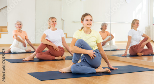 Young positive teenager girl doing stretching workout during group training in yoga class
