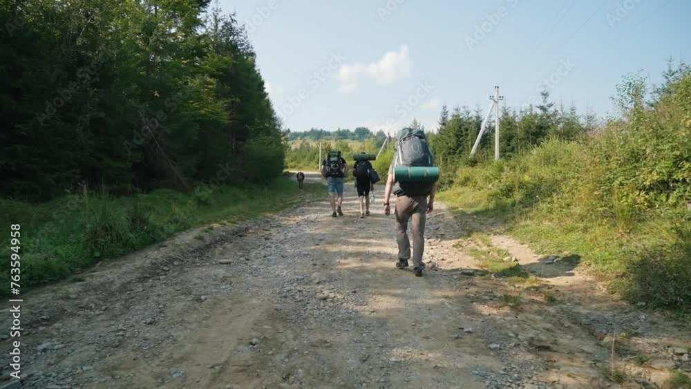 A group of tourists with backpacks climbs the mountain on a dirt road. Mountain climbing, nature, good natural conditions in the mountains. A group of tourists with backpacks climbs the mountain on a dirt road. Mountain climbing, nature, good natural conditions in the mountains.