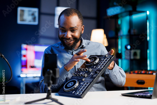 Smiling BIPOC artist filming DJ mixing tutorial in recording studio, playing with turntables, samples and sound effects. Music production content creator showcasing audio equipment to audience