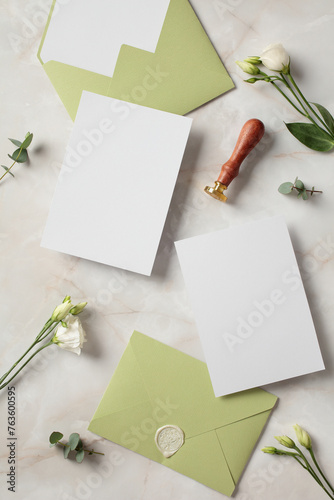 Blank wedding invitation cards, envelopes, flowers and wax stamp on stone table. Flat lay, top view, copy space.