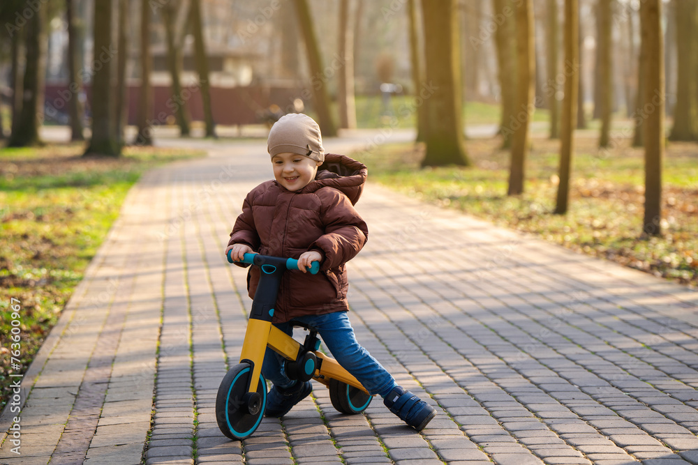 A cute toddler boy of three years old rides a bicycle or balance bike in a city park on a spring summer day. Toddlerhood and childhood concept. Active leisure A cute toddler boy of three years old rides a bicycle or balance bike in a city park on a spring summer day. Toddlerhood and childhood concept. Active leisure