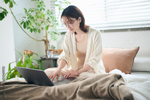 ベッドでノートパソコンを使う20代女性