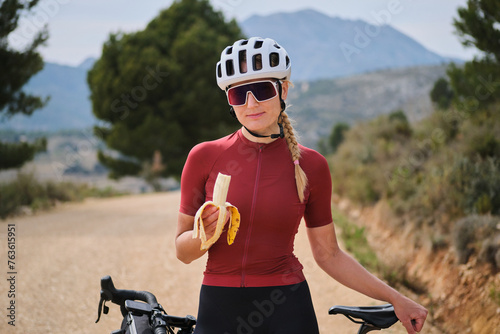 A woman cyclist holding a banana with a background of a red cycling jersey. Healthy nutrition of a cyclist. Healthy snack for a cyclist during training. 