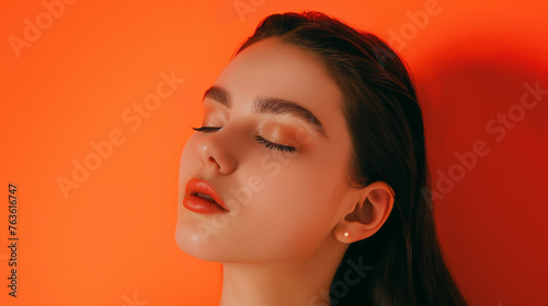 Close up no rosto de uma modelo de olhos fechados isolado no fundo laranja  photo