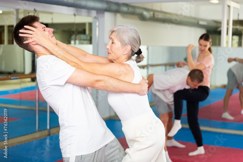 Determined elderly woman attacking eyes of male sparring partner as self-defense tactic during workout in practice hall
