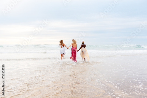 multiracial group of friends run together along the beach shore on a summer day