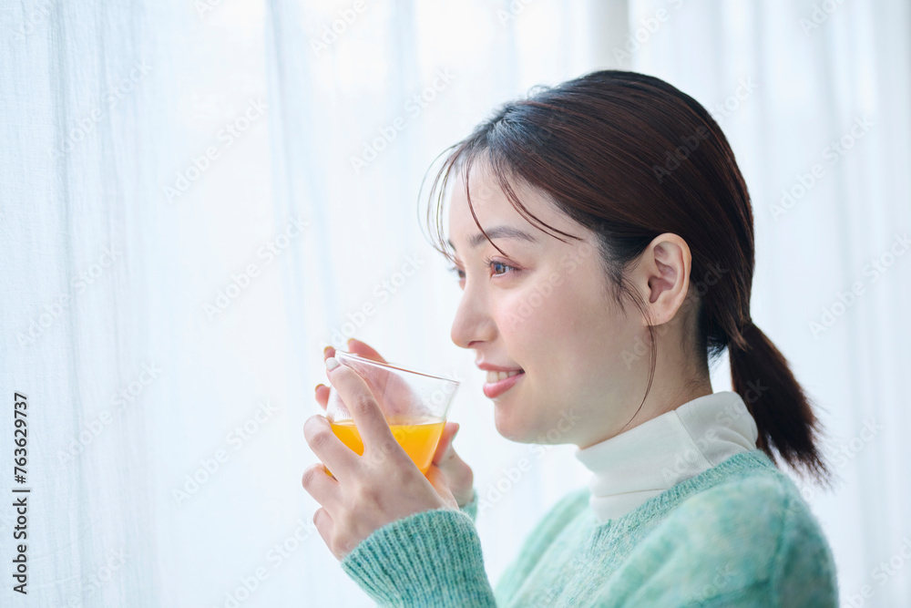 窓際でオレンジジュースを飲む20代女性 窓際でオレンジジュースを飲む20代女性