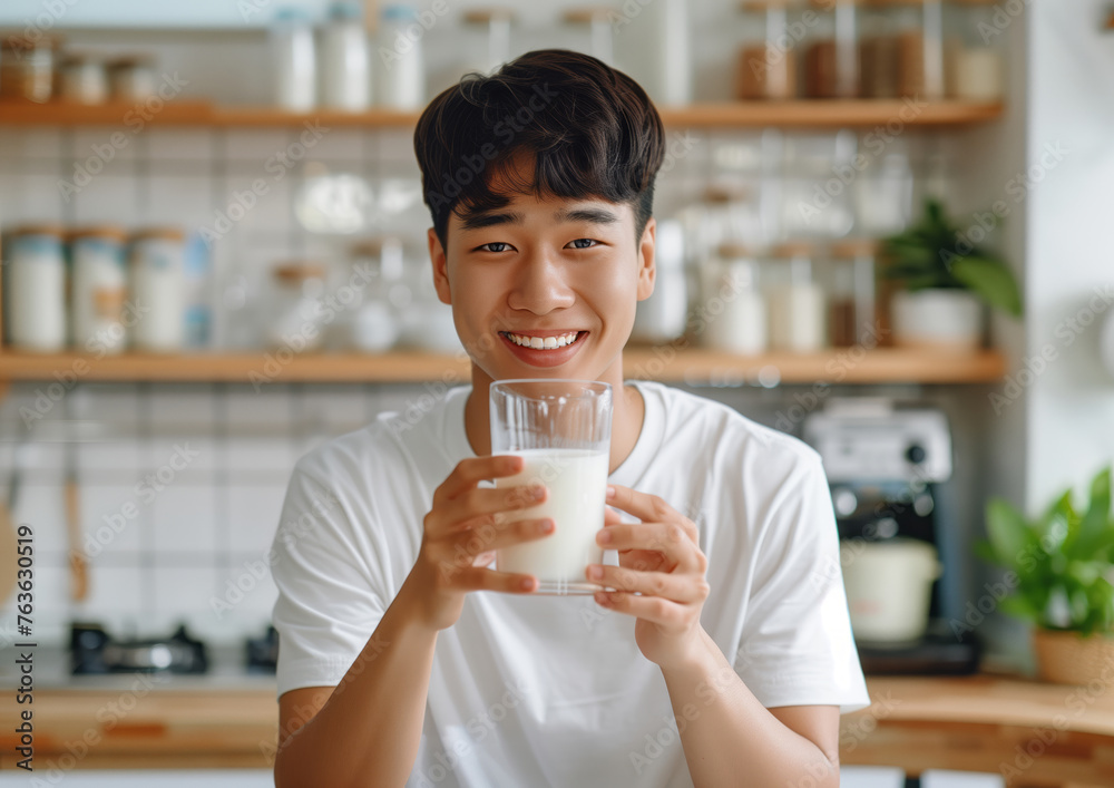 Happy Asian man in the light modern kitchen drinking milk from the glass Happy Asian man in the light modern kitchen drinking milk from the glass