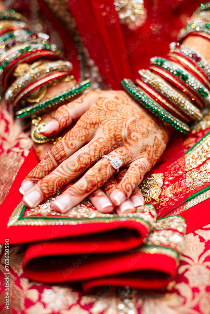 Indian bride with henna tattoo rests hands on red and green sari