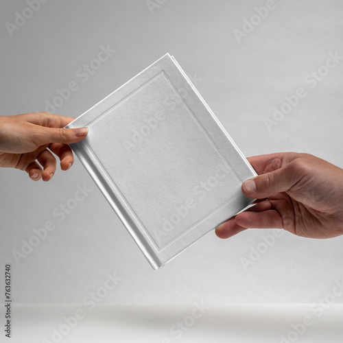 Male and female hands holding a blank notebook. Hardcover book. Matte white. Blank book mockup. Textured paper. (real photo) 3D render dots in background.  (ID: 763632740)