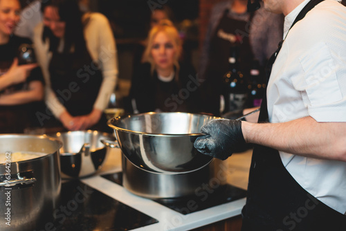 Group of guests in a cooking class studio, adults preparing different dishes in the kitchen together, people in aprons learn on culinary master class, chef uniform, hands in gloves, italian cuisine photo