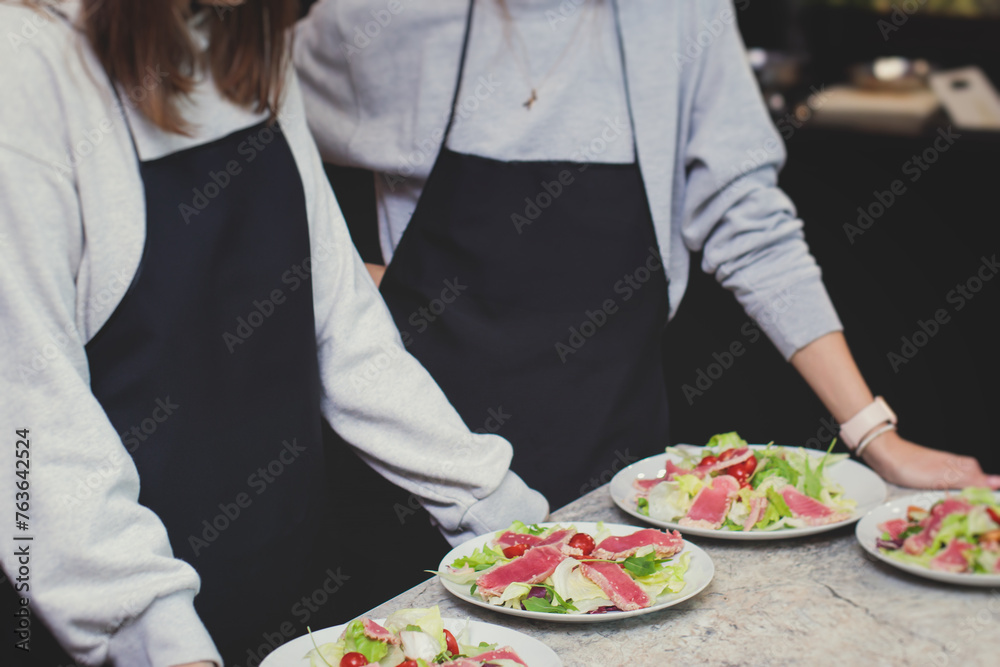 Group of people in a cooking class studio, adults preparing different dishes in the kitchen together, people in aprons learn on culinary master class, chef uniform, hands in gloves, italian cuisine Group of people in a cooking class studio, adults preparing different dishes in the kitchen together, people in aprons learn on culinary master class, chef uniform, hands in gloves, italian cuisine