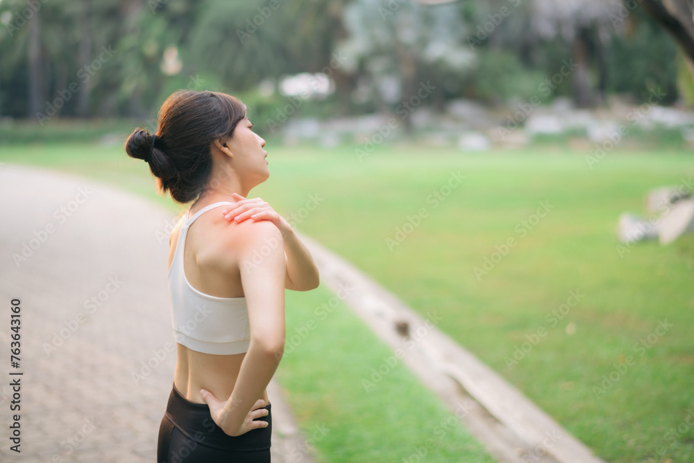 Shoulder pain problem. woman jogger. 30s asian female wearing white sportswear holding her shoulder with pain after running exercise in public park. Shoulder pain problem. woman jogger. 30s asian female wearing white sportswear holding her shoulder with pain after running exercise in public park.