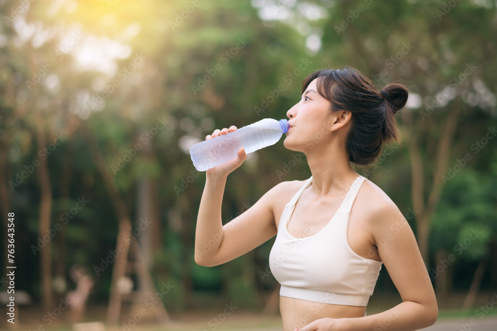 Female runner. Fit Asian young woman with white sportswear drinking water after running and enjoying a healthy outdoor. Fitness runner girl in public park. Wellness being concept Female runner. Fit Asian young woman with white sportswear drinking water after running and enjoying a healthy outdoor. Fitness runner girl in public park. Wellness being concept