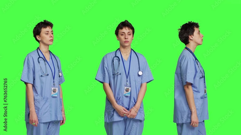 Young nurse with medical expertise poses with confidence, wears blue scrubs uniform and smiling against greenscreen backdrop. Health assistant gives support to doctors as profession. Camera B. Young nurse with medical expertise poses with confidence, wears blue scrubs uniform and smiling against greenscreen backdrop. Health assistant gives support to doctors as profession. Camera B.
