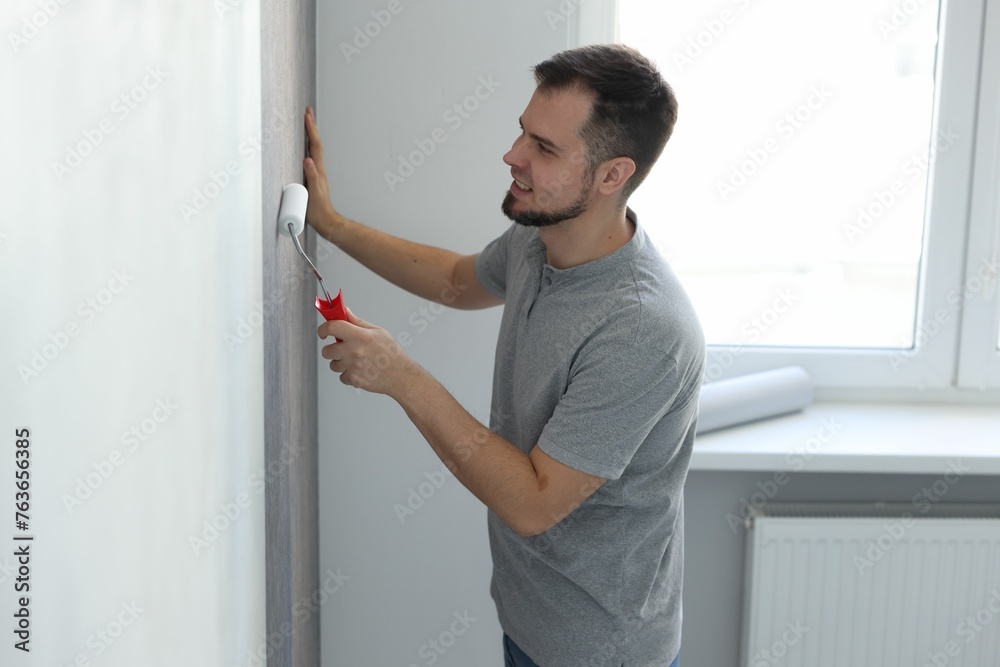 Man hanging stylish gray wallpaper in room Man hanging stylish gray wallpaper in room