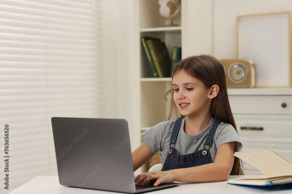 Cute girl using laptop at white table indoors