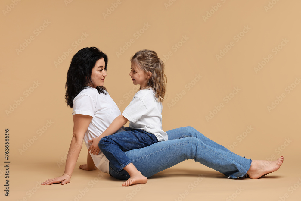 Beautiful mother with little daughter sitting on beige background Beautiful mother with little daughter sitting on beige background