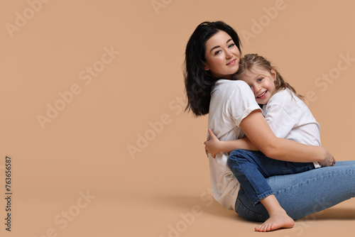 Beautiful mother with little daughter sitting on beige background. Space for text © New Africa