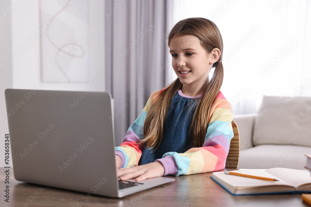 E-learning. Cute girl using laptop during online lesson at table indoors E-learning. Cute girl using laptop during online lesson at table indoors