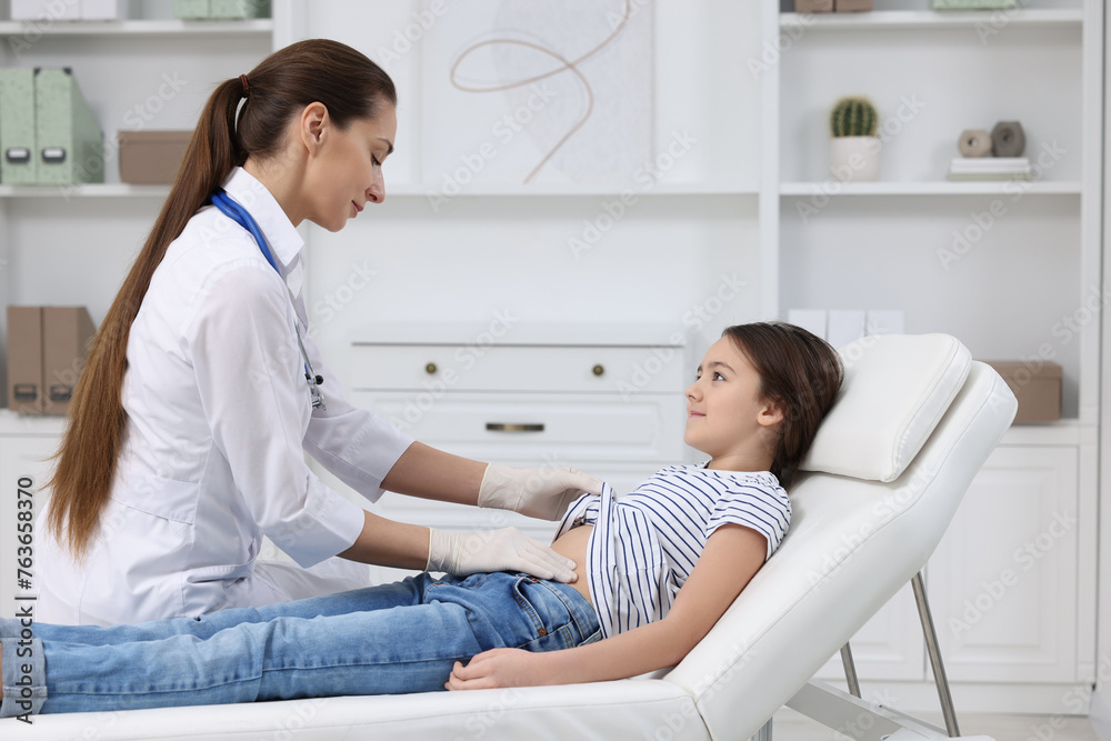 Gastroenterologist examining girl with stomach ache on couch in clinic