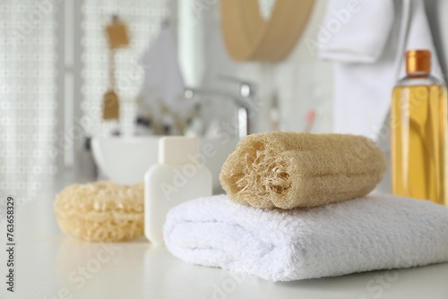 Natural loofah sponge and towel on table in bathroom. Space for text