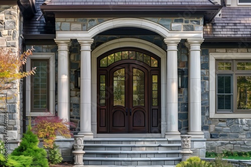 The grand entrance to the building features a large stone house with brickwork, a spacious porch, and a fixture of a front door overlooking a lush green residential area