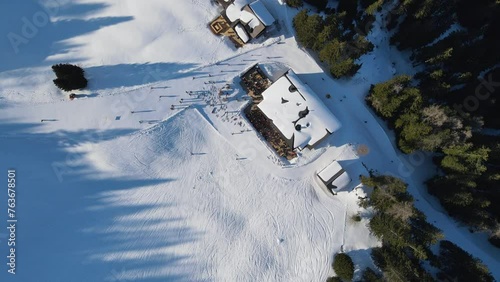 Aerial: Birds Eye View, Drone flying Down to a Ski-Bungalow, surrounded by a slope with skking people photo