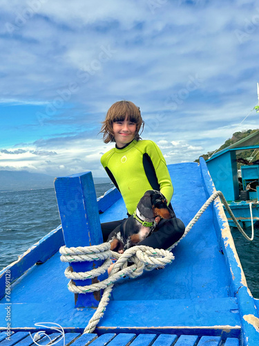 A boat trip. Smiling young girl sitting on the bow of a boat with a dog (ID: 763691128)