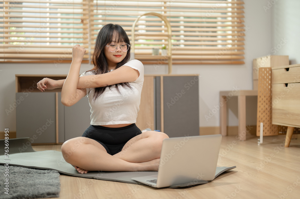 A fit woman is stretching her body on a yoga mat while watching an online yoga tutorial video. A fit woman is stretching her body on a yoga mat while watching an online yoga tutorial video.