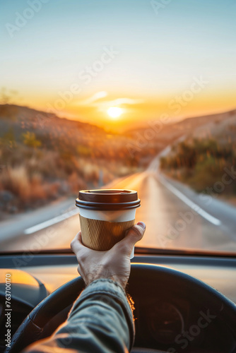 Young man enjoying scenic sunrise while driving with coffee to go cup on beautiful road